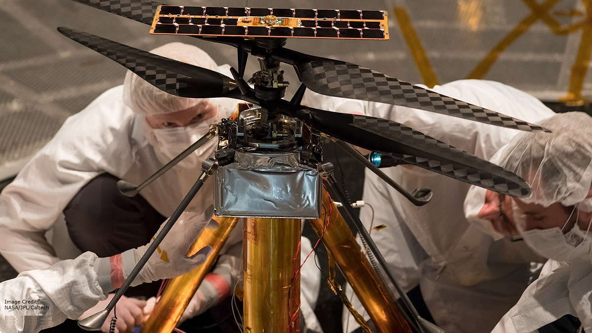 Image: Two experts in protective suits examine a rotor drone with a gold-plated center section and four carbon fiber-reinforced rotor blades.